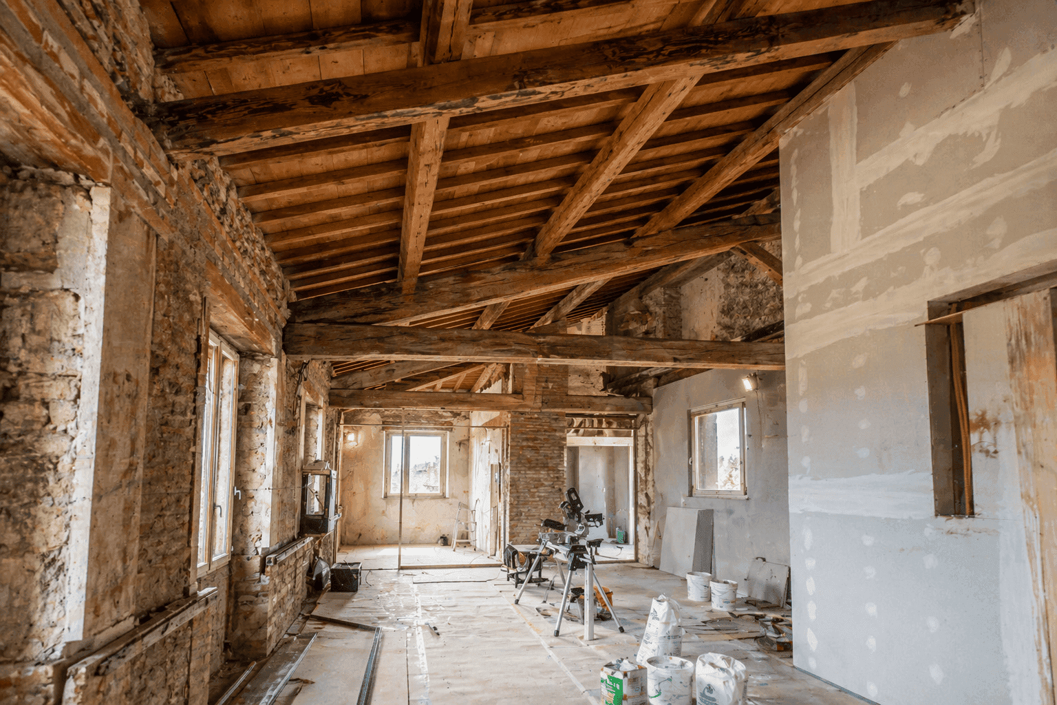 Interno di edificio in fase di rifacimento con travi in legno a vista, pareti in pietra e cartongesso